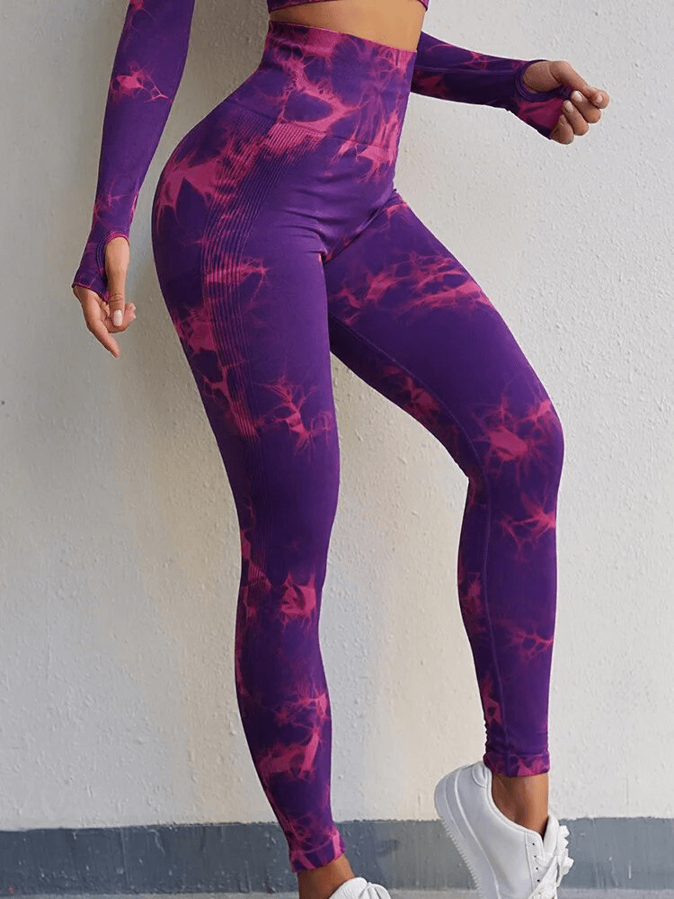 Woman wearing purple tie-dye high-waisted sport leggings next to white wall